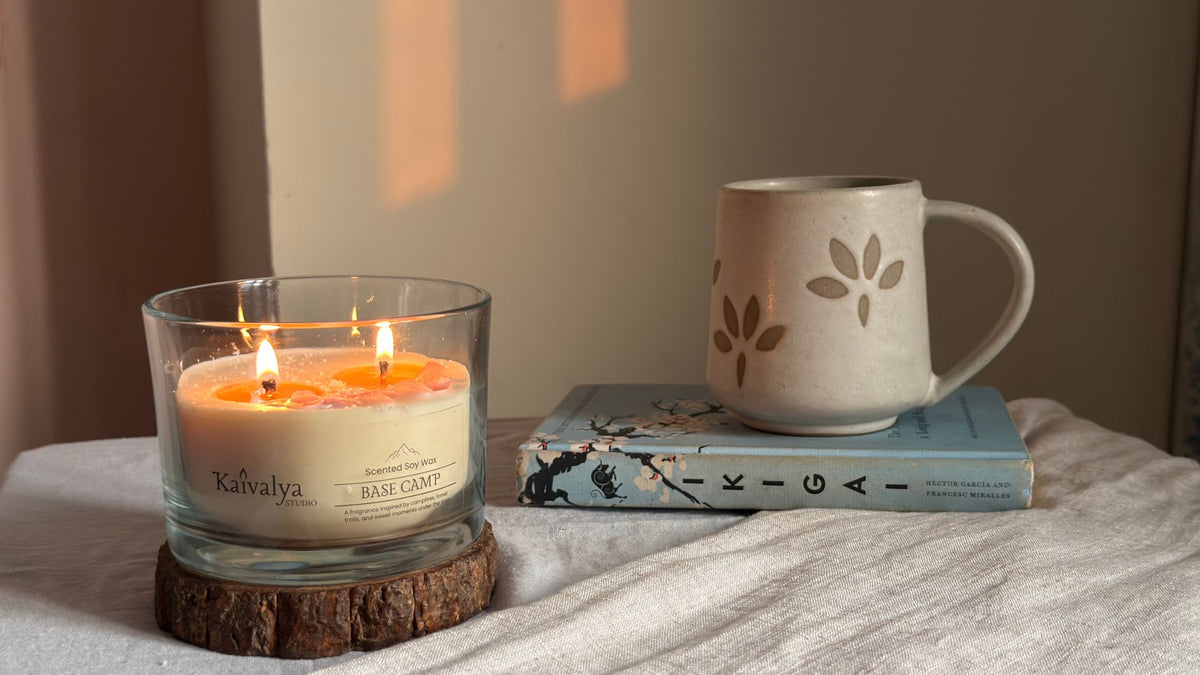 Hand-poured Base Camp soy candle styled with a coffee mug, natural stones and greenery in a warm, rustic setting. 
Luxury soy candle in the Base Camp fragrance creating a calm and cozy atmosphere with natural décor and warm lighting.